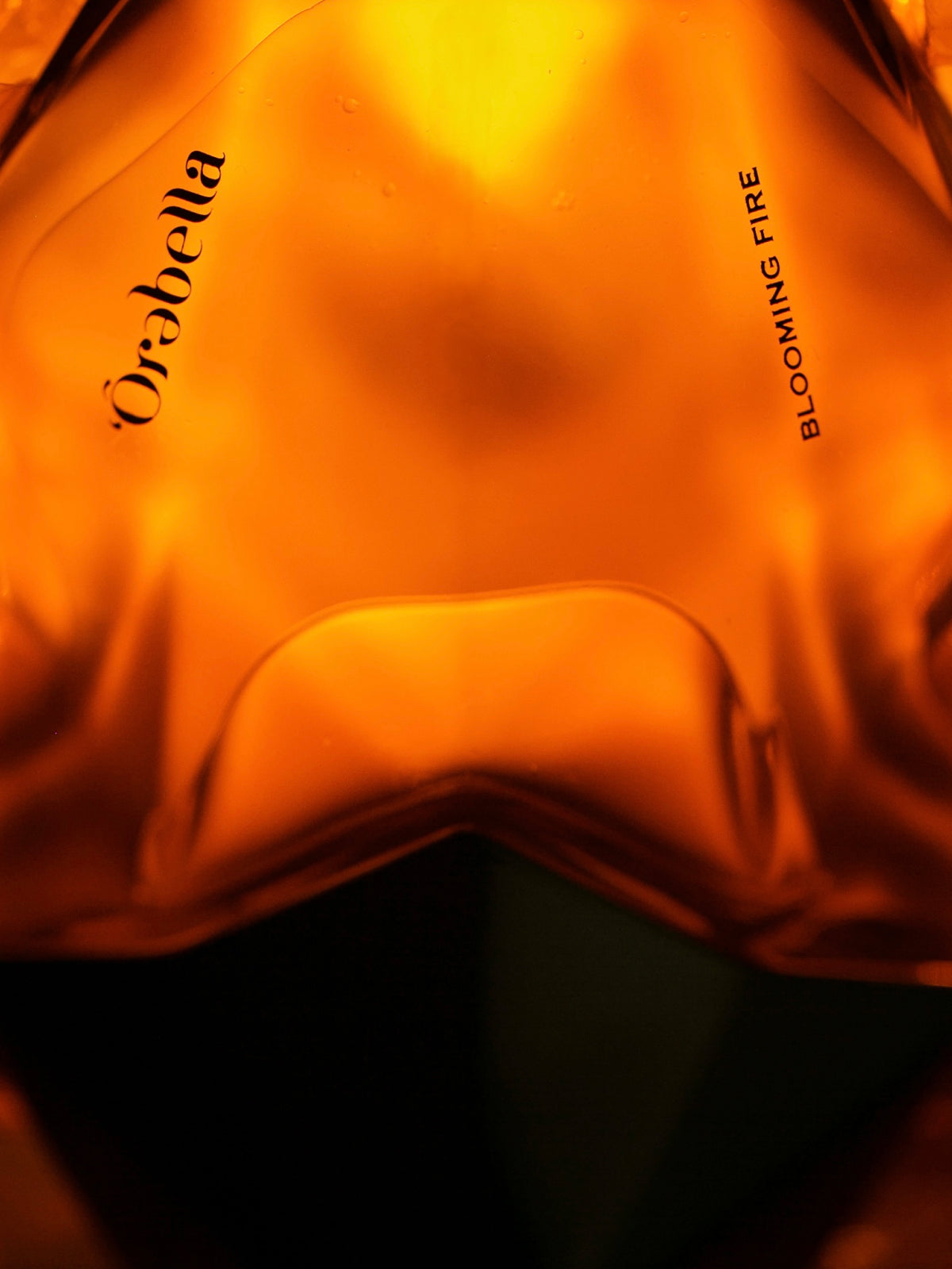 Close-up of a warm amber-orange translucent bottle or container with the brand name 'Orbella' printed in black script on the front.