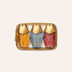 A three-piece hair care set by Orebella, including Golden Brulee, Nectar Dew and Gardenia's Whisper bottles, arranged inside a transparent zippered pouch with a gold trim, on a light beige background.