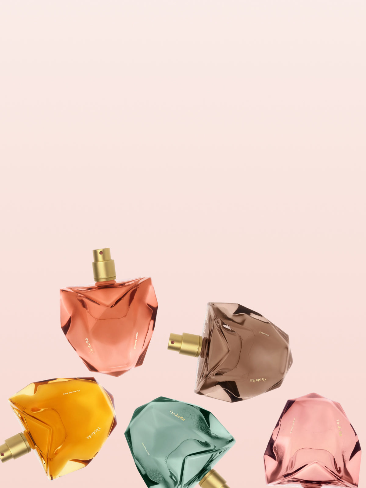Five Orebella perfume bottles in shades of bronze, gold, green, pink, and red arranged on a light blush pink background.