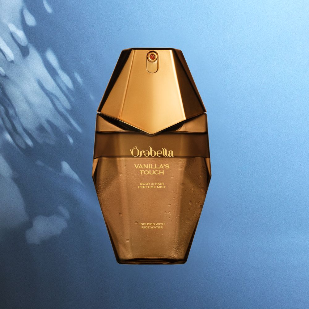 A faceted metallic gold perfume bottle labeled 'Orbella Vanilla's Touch' centered against a blue gradient background with soft light streaks.