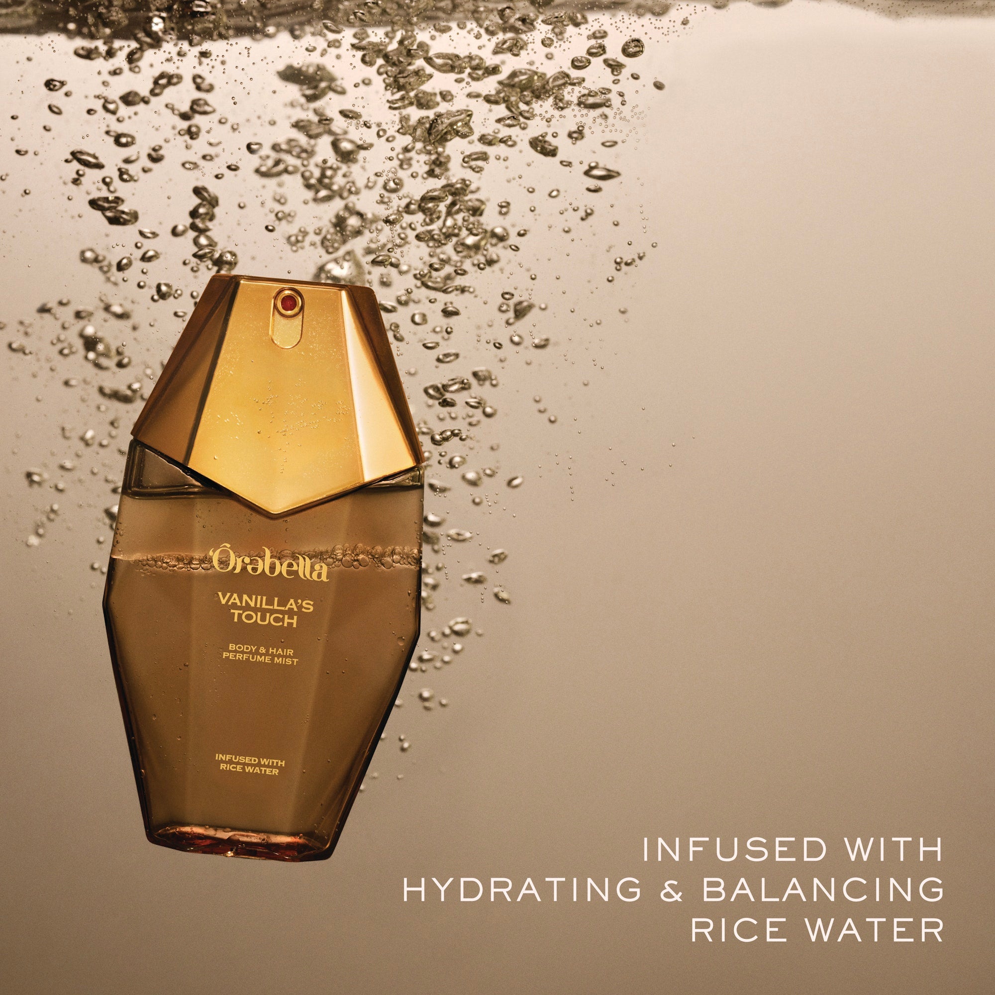 Orabella Vanilla's Touch perfume bottle floating in water with bubbles around it, set against a warm beige background with text reading 'INFUSED WITH HYDRATING & BALANCING RICE WATER'.
