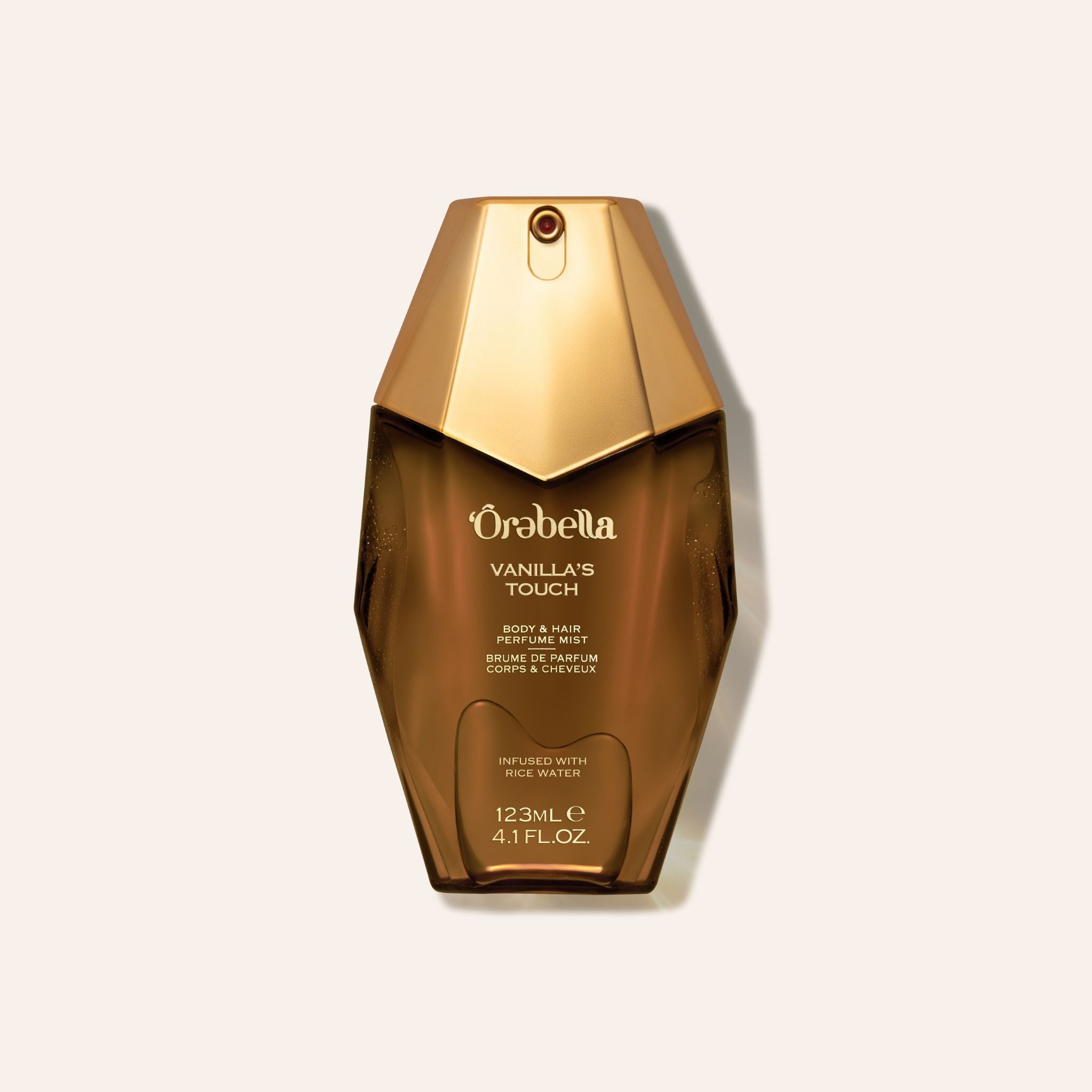 A bottle of Orabella Vanilla Touch body wash in a faceted metallic gold bottle, centered on a light beige background.