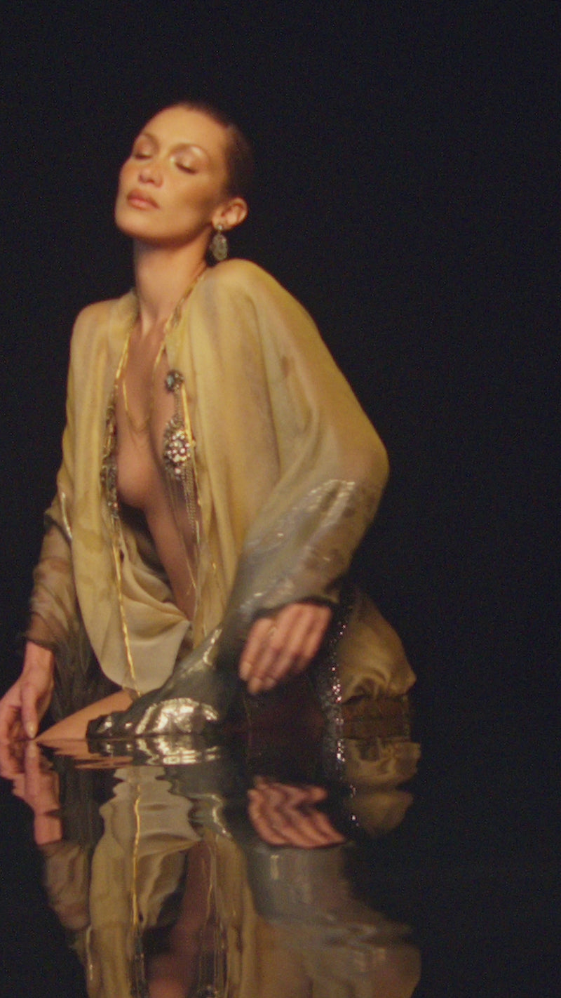 Bella Hadid posing gracefully in a sheer golden outfit for the Orebella Vanilla's Touch campaign video.