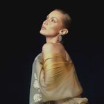 Bella Hadid posing gracefully in a sheer golden outfit while spraying Vanilla's Touch Body & Hair Perfume mist in campaign video 