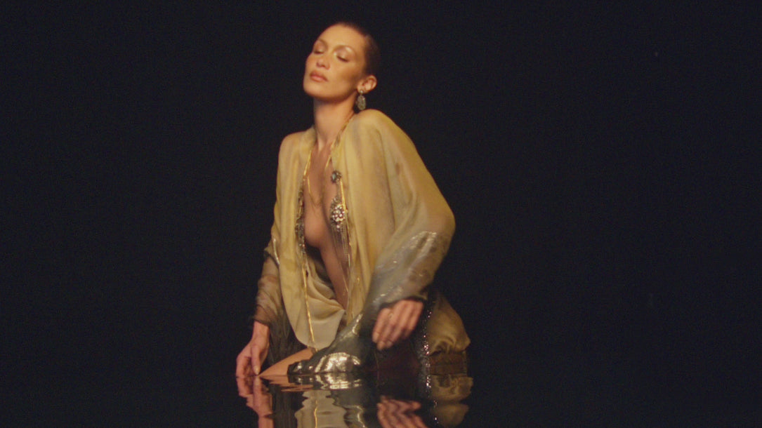 Bella Hadid posing gracefully in a sheer golden outfit for the Orebella Vanilla's Touch campaign video.